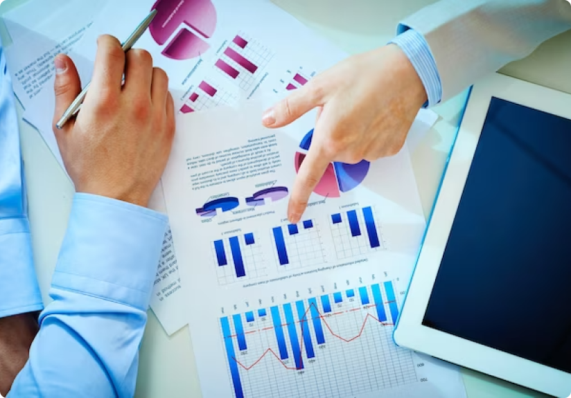 Two people discuss graphs and charts printed on paper, analyzing information with a tablet nearby, evaluating potential risk factors.