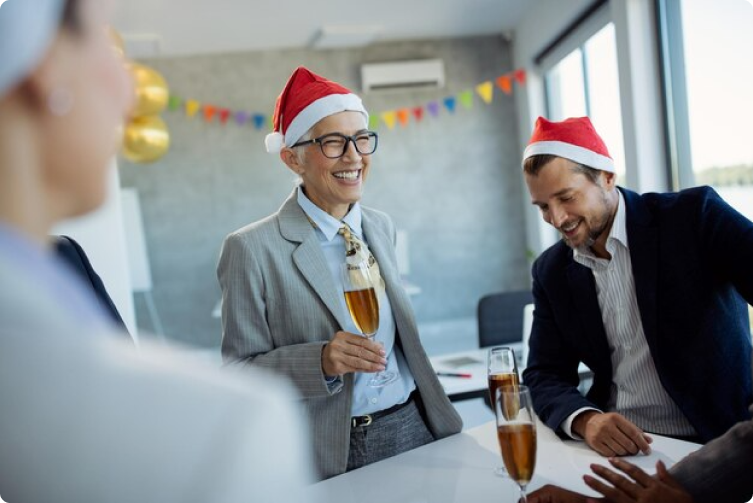 People wearing Santa hats and business attire gather around a table reducing the risk of work stress.