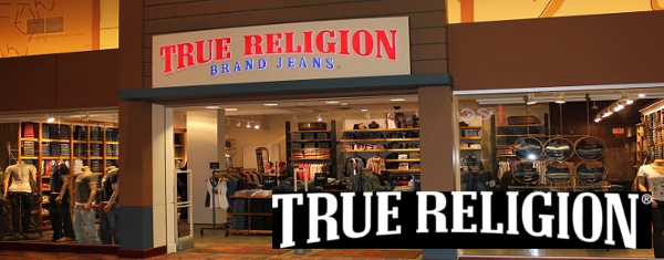 Exterior view of a True Religion Brand Jeans store with a large sign above the entrance and jeans displayed inside, showcasing premium consumer products.