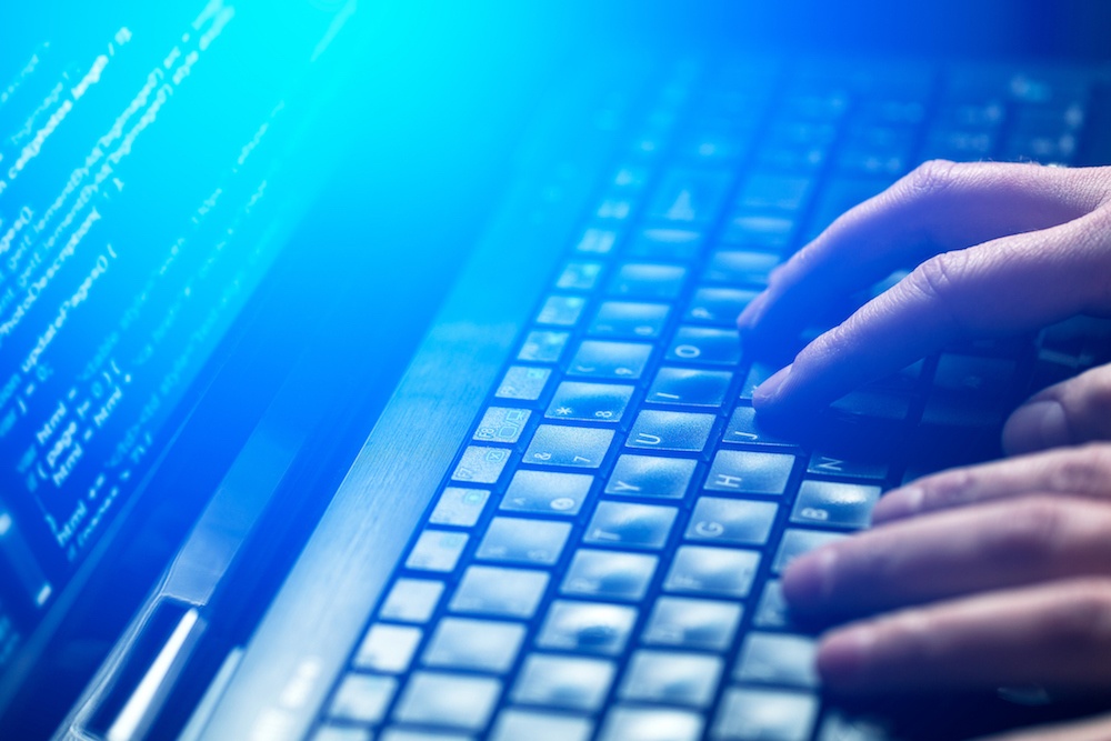 Close-up of hands typing on a laptop keyboard with code displayed on the screen.