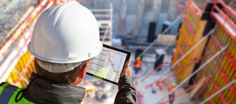 A construction worker wearing a hard hat and reflective vest uses a tablet on a building site, meticulously fortifying foundations.