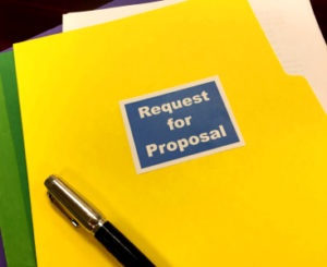 Yellow folder labeled "Request for Proposal" with papers inside and a pen resting on it.