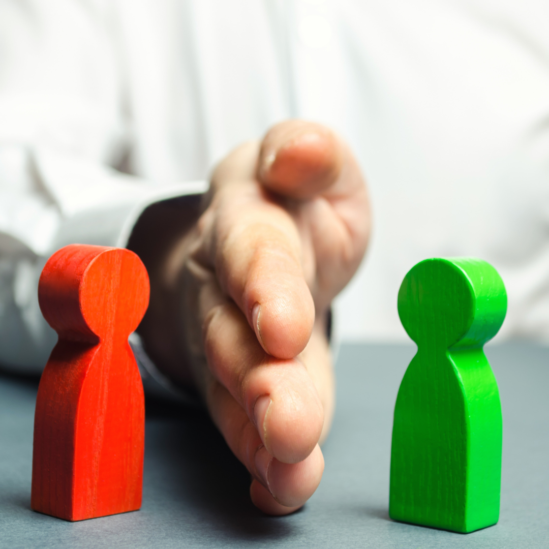 A hand is placed vertically between a red wooden figure on the left and a green wooden figure on the right, symbolizing corporate principles of separation or mediation.