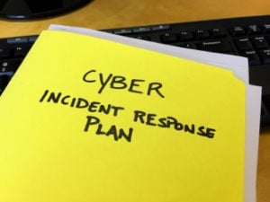 A yellow folder labeled "Cyber Incident Response Plan" lies on a desk near a computer keyboard.