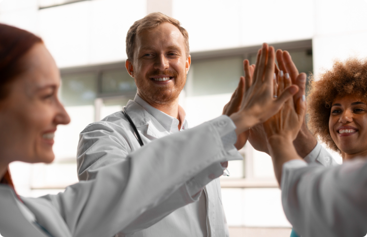 A group of medical professionals, wearing white coats, gather together for a high five outside a building