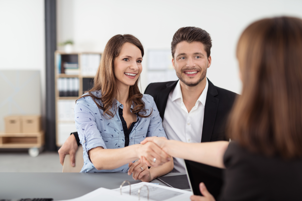 A smiling couple sits at a desk, shaking hands with another person discuss the future of their Florida enterprise's risk management.