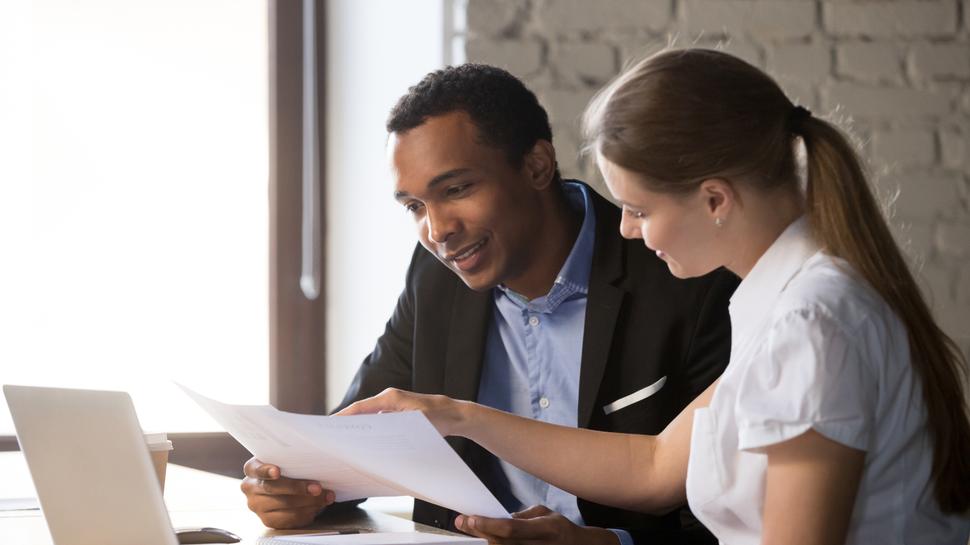 Two people are sitting at a desk, reviewing a healthcare benefits document together near a laptop.