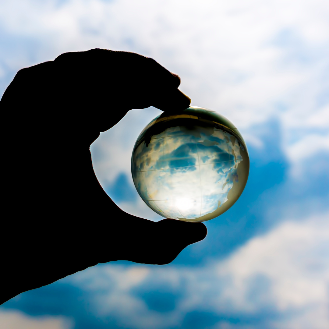 A hand holds up a transparent sphere against a cloudy sky