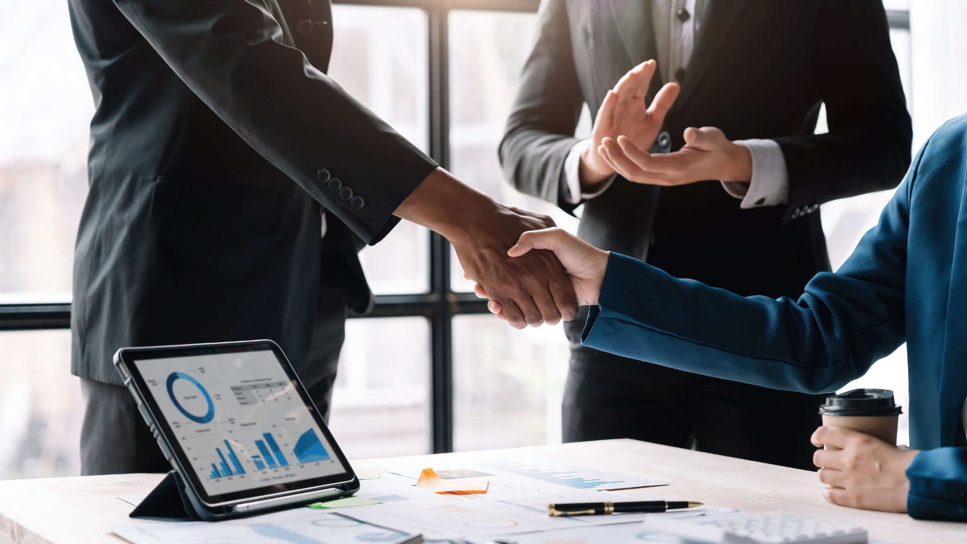 Business people shake hands over a table, underscoring the pivotal role of a Mergers and Acquisitions consultant in facilitating the deal.