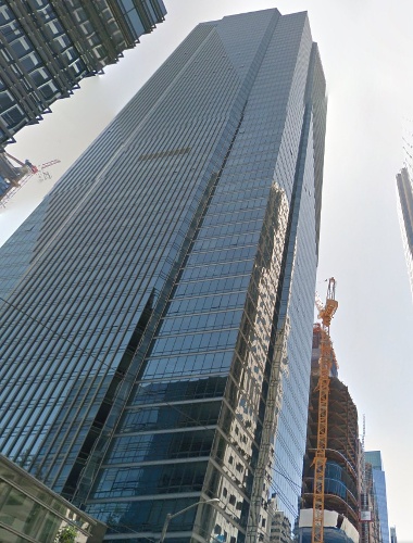 Tall glass and steel skyscraper with reflective windows, surrounded by construction cranes