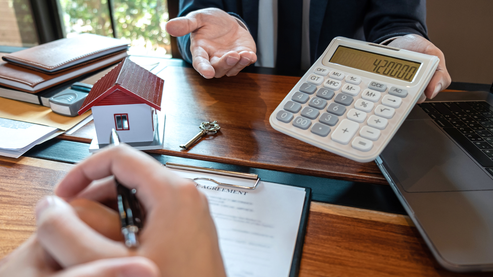 A person holds a calculator, while another person writes on a document assessing the Total Cost of Risk.