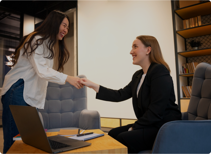 Two women shaking hands in an office setting—a perfect snapshot of a day in the life at this dynamic workplace.