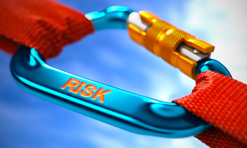 A blue carabiner labeled "RISK" is attached to a red strap, symbolizing the importance of risk management, all set against a bright sky in the background.