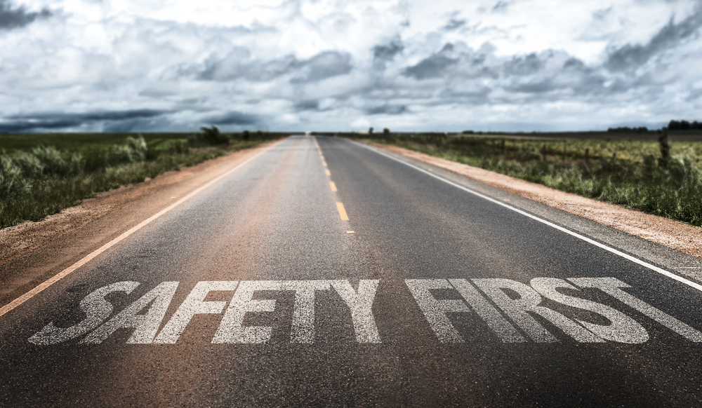 Empty rural road with "SAFETY FIRST" painted in large white letters on the asphalt, cloudy sky overhead.