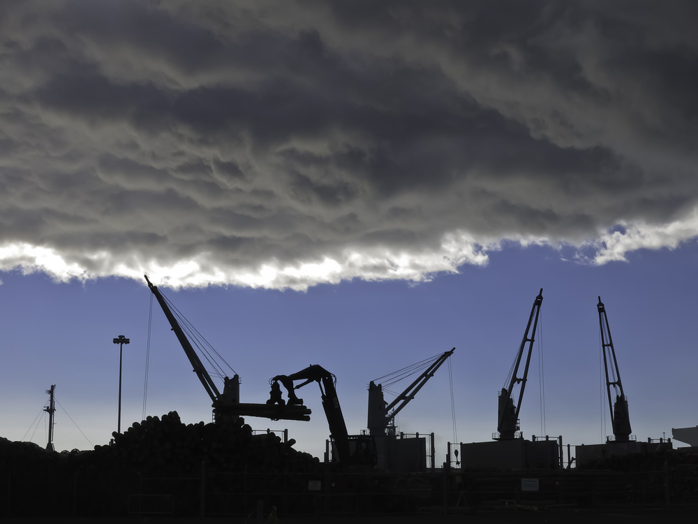 Storm cloud over silhouettes of cranes lifting logs to be shipped from seaport of Astoria, Oregon