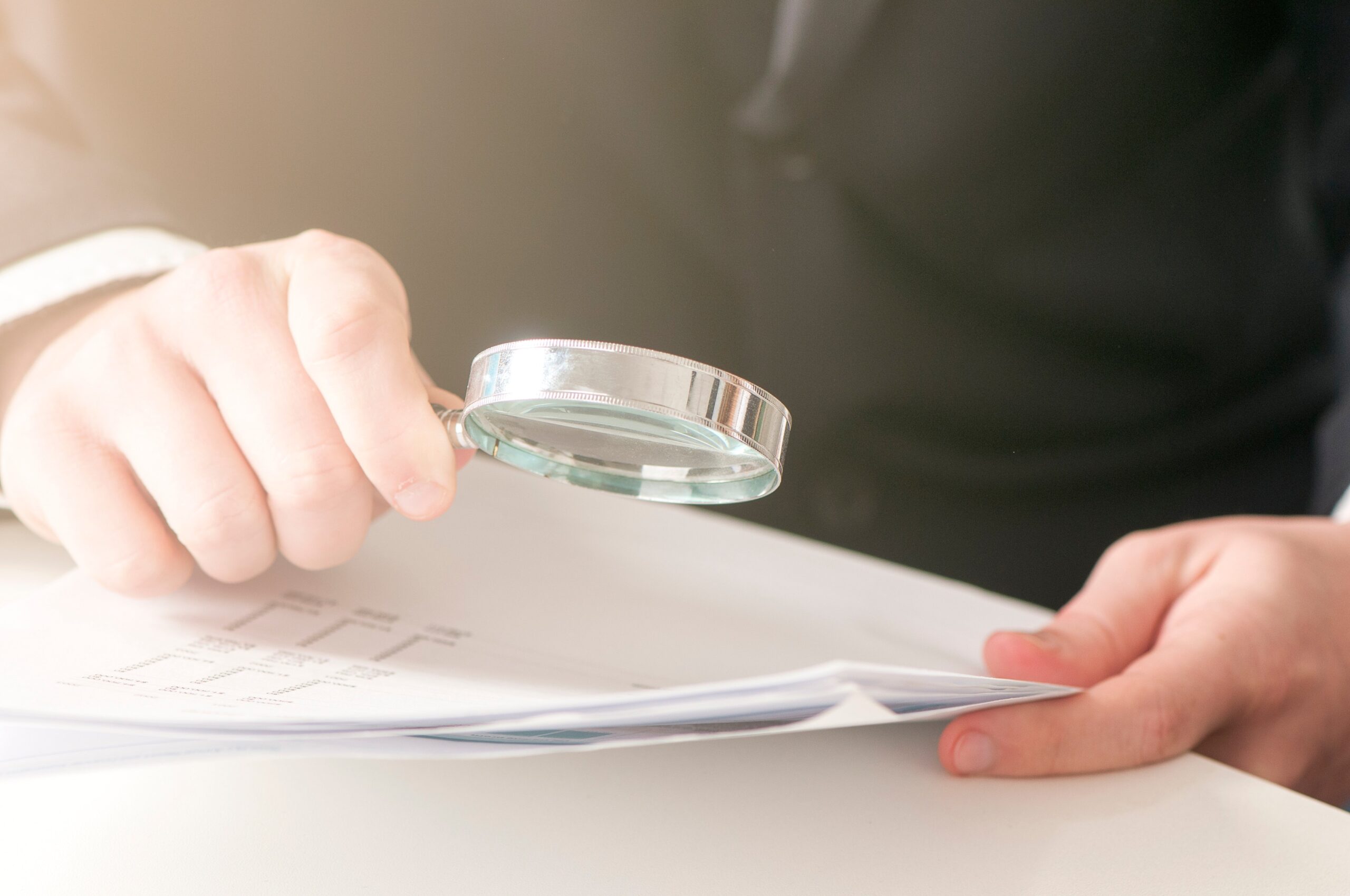 A person holding a magnifying glass over a stack of documents.