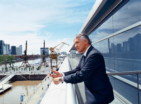 A risk management consultant in a suit stands on a modern balcony, holding a smartphone