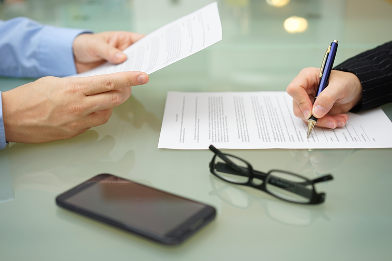 Two people review and sign risk management documents on a glass table