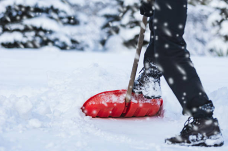 Person shoveling snow with a red shovel, wearing black pants and boots