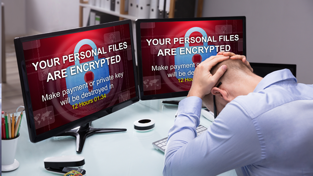 A person sits at a desk with their head in their hands displaying a ransomware message highlighting the severe consequences of cyber risk.