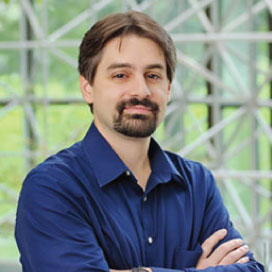 Man with beard and mustache, wearing a blue shirt, appears to be a risk management consultant confidently assessing his surroundings.