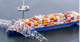 A cargo ship loaded with multicolored containers lies trapped beneath a collapsed metal structure in the water. This situation calls for an immediate risk assessment to prevent further damage and ensure safety protocols are followed.