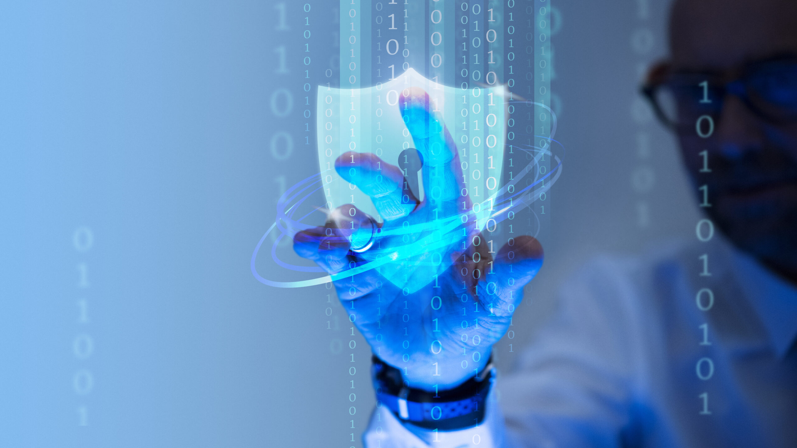 A person touches a shield icon hologram surrounded by binary code, symbolizing Smart Equipment Cybersecurity and data protection.