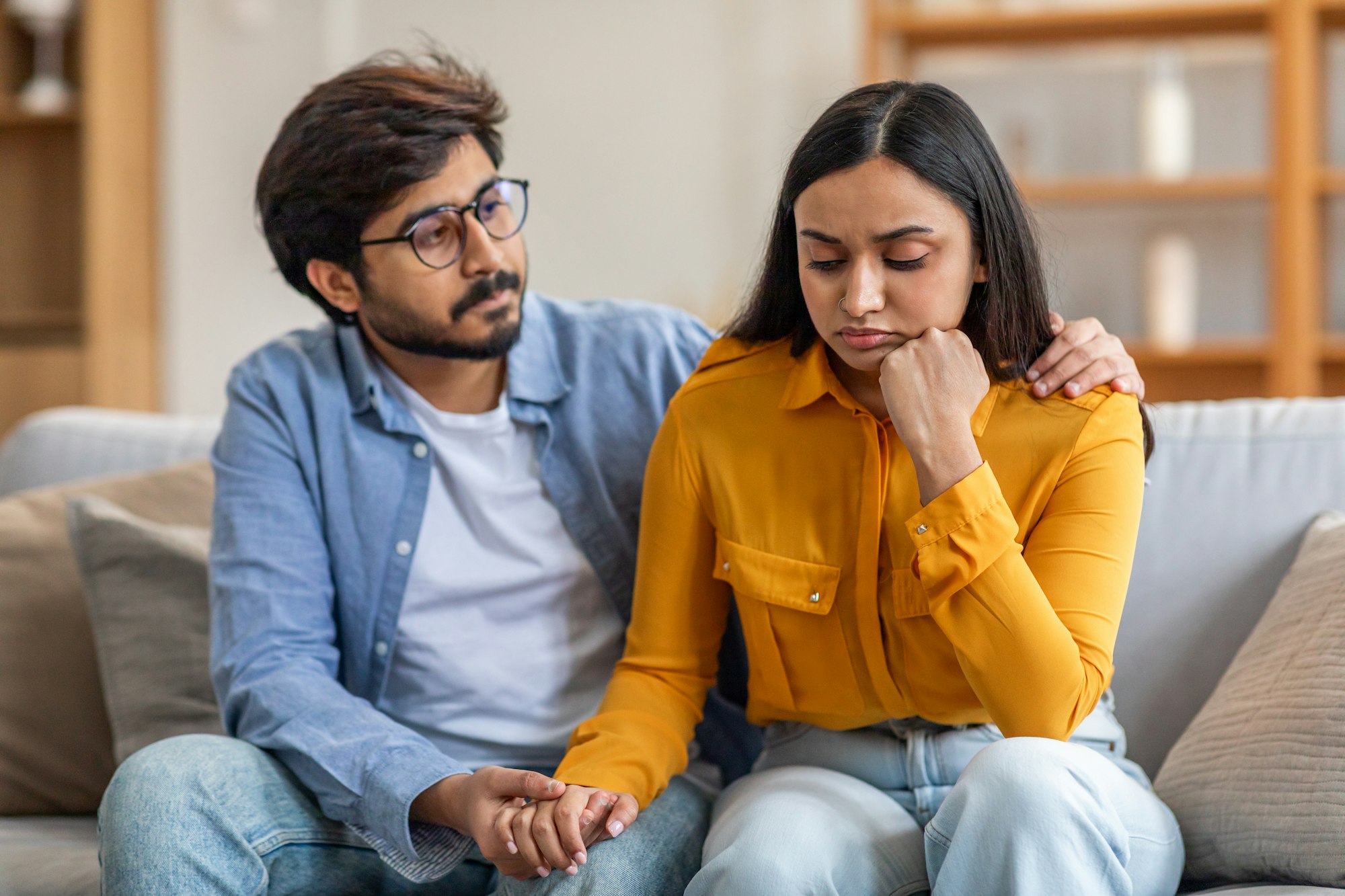 Concerned Man Comforts Upset Woman on Couch During Daytime